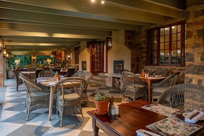 A restaurant with wicker furniture, stone walls, and a checkered floor. - Walkersons Hotel Spa (Dullstroom)