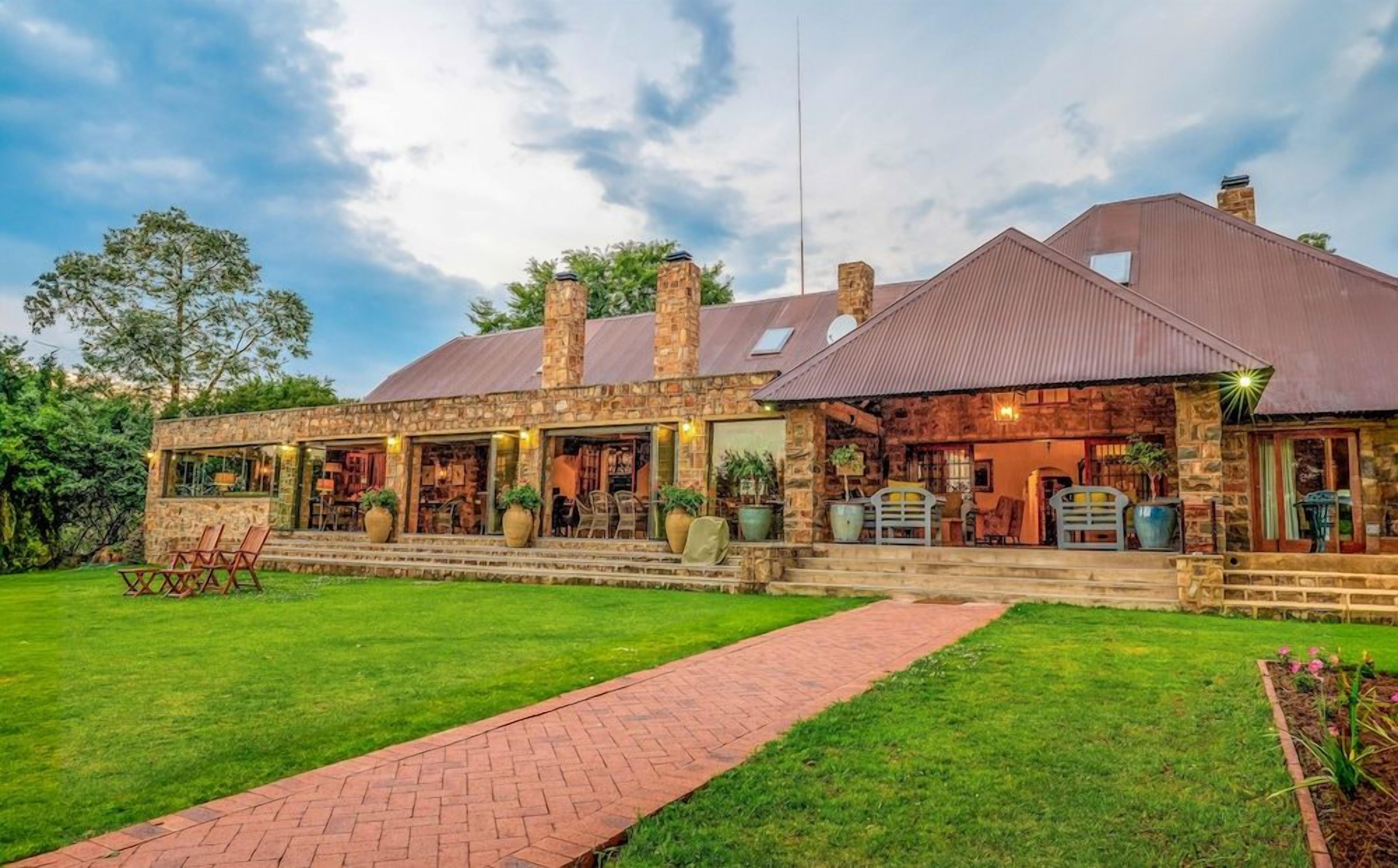 A two-story stone building with a covered patio area, outdoor seating, and a brick pathway leading to the entrance.