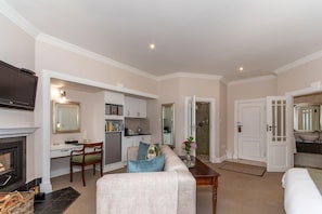 A living room with a fireplace, a television, a sofa, a coffee table, and a kitchen area. - Walkersons Hotel Spa (Dullstroom)