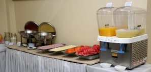 Disposição de buffet com diversos alimentos e um dispensador de suco.