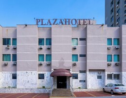 Un edificio con un cartel que dice 'PLAZAHOTEL' sobre la entrada, con fachada plana y múltiples ventanas y unidades de aire acondicionado.