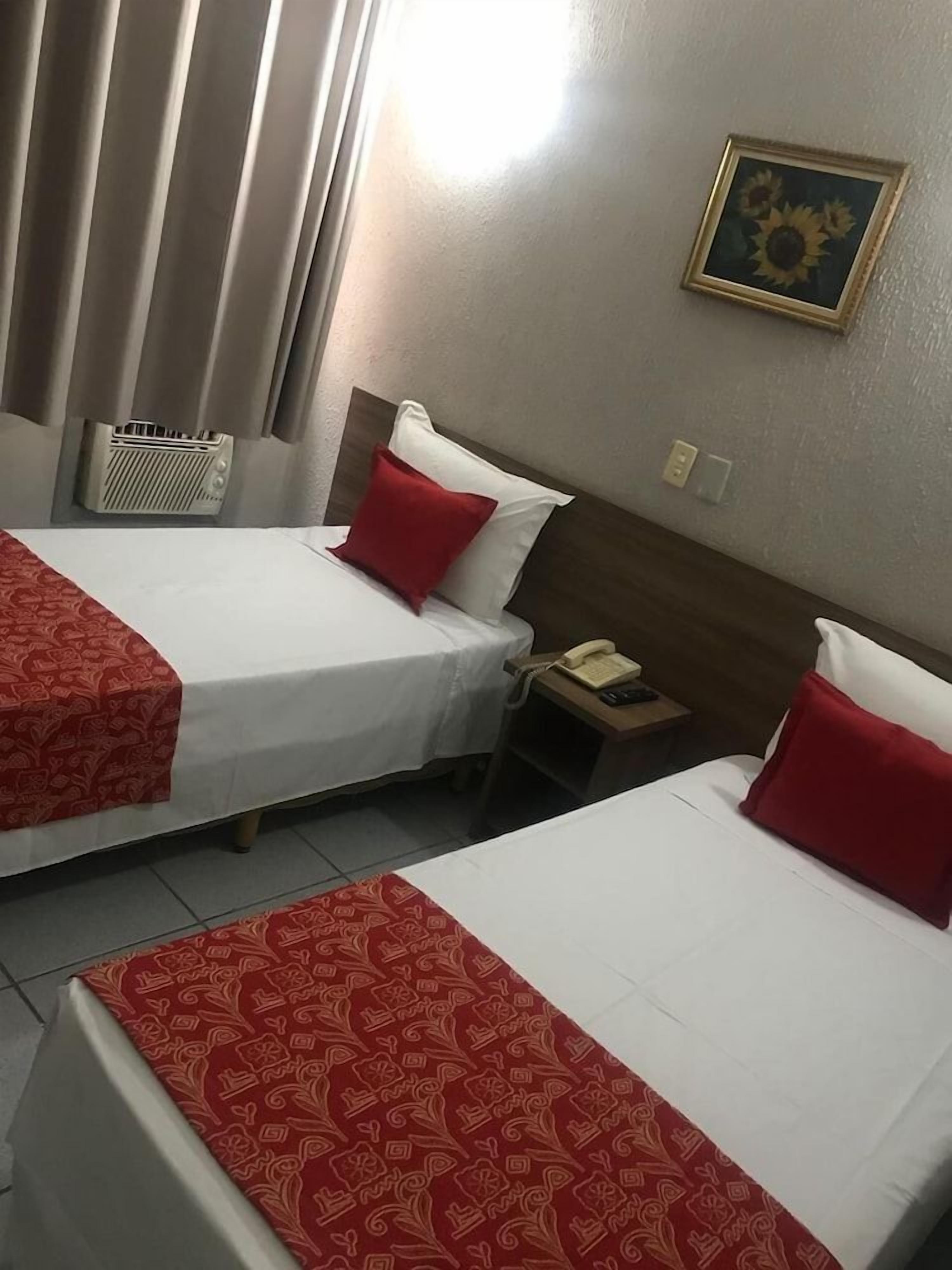 Two single beds with red and white bedding, a bedside telephone, and a wall-mounted picture frame.