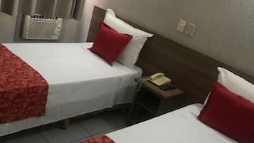 Duas camas de solteiro com roupa de cama vermelha e branca, um telefone ao lado da cama e um quadro pendurado na parede.