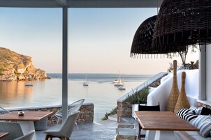 Una terraza frente al mar con mobiliario exterior, un muro de piedra y vistas a barcos en el agua.