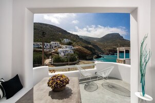 Un balcón con vistas a un pueblo costero, mobiliario blanco y una planta decorativa.