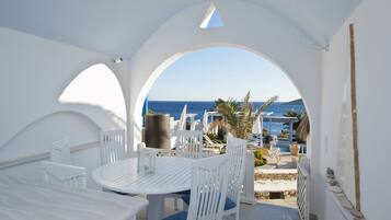 A white outdoor seating area with a table and chairs, overlooking a pool and the sea.