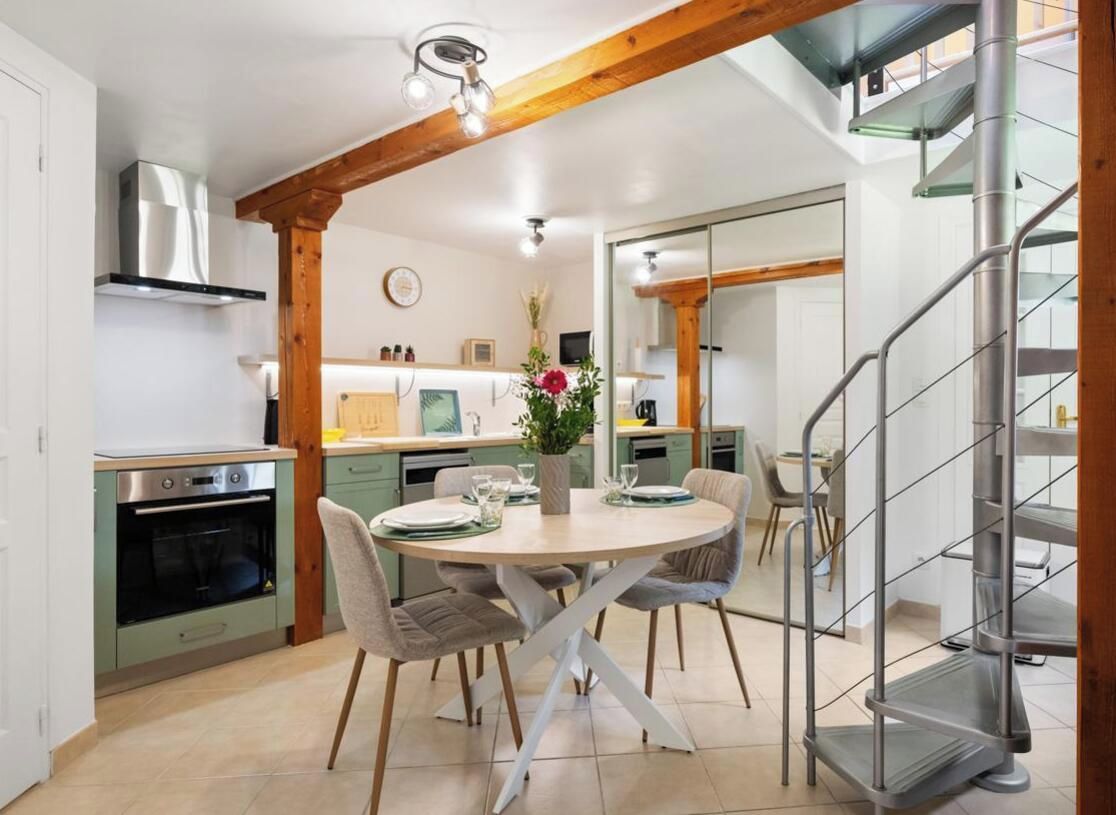 A modern kitchen with a dining area, featuring a round table, chairs, and a staircase.