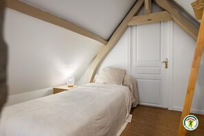 A bedroom with a sloped ceiling, a bed, a bedside table with a lamp, and a door. - Gîtes de France® - Le Colibri (LONGROY)