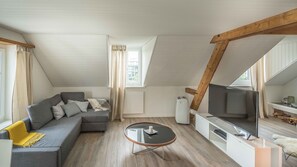 A modern loft apartment with a sloped ceiling, a grey sectional sofa, a glass coffee table, a flat-screen TV, and a white built-in entertainment unit. - Löwenplatz Apartment Near Station by Airhome (Zürich)