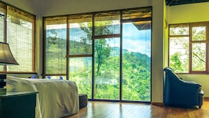 A room with a bed, a chair, and large windows with a view of a forest. - The Tea Cottage Resort And Spa (Sri Lanka)