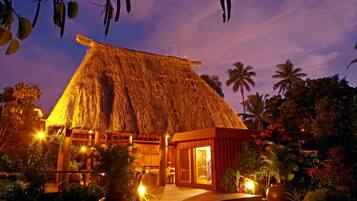 A thatched-roof building with a wooden veranda, surrounded by tropical vegetation.