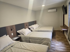 Quarto de hotel com três camas de solteiro, piso de madeira, ar-condicionado fixado na parede e televisão na parede.