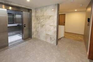 Een moderne lift met een metalen afwerking, een marmeren wand met een subtiel patroon en een houten deur met nummerbord.