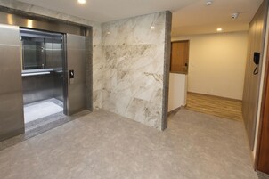 Un ascensor moderno con detalles metálicos, una pared de mármol con un diseño sutil y una puerta de madera con una placa de número.