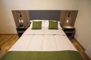 Une chambre d’hôtel avec un grand lit, deux tables de chevet, un téléphone et un luminaire fixé au mur.
