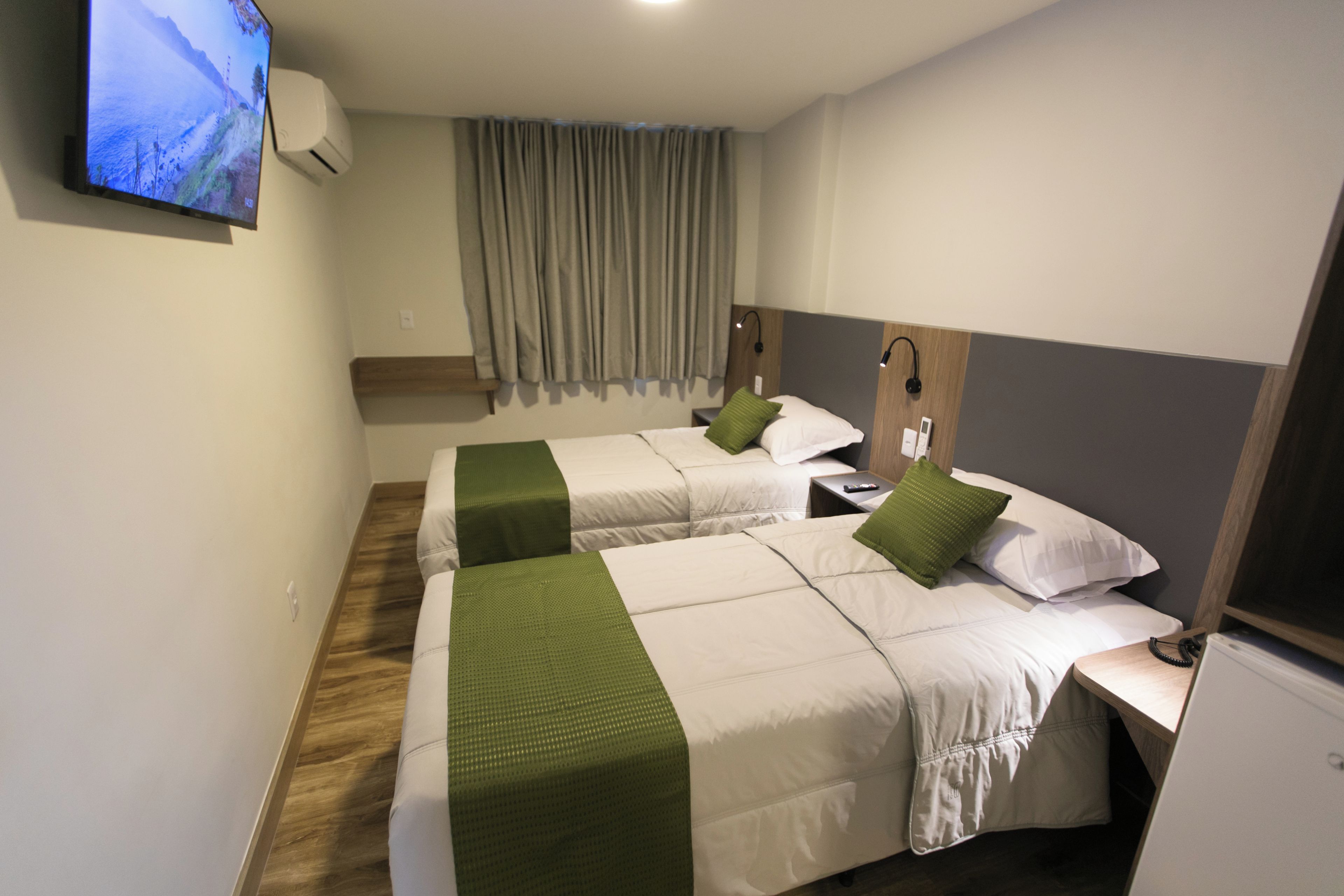 Ein Hotelzimmer mit zwei Betten, einem Fernseher, einer Klimaanlage und Holzboden.