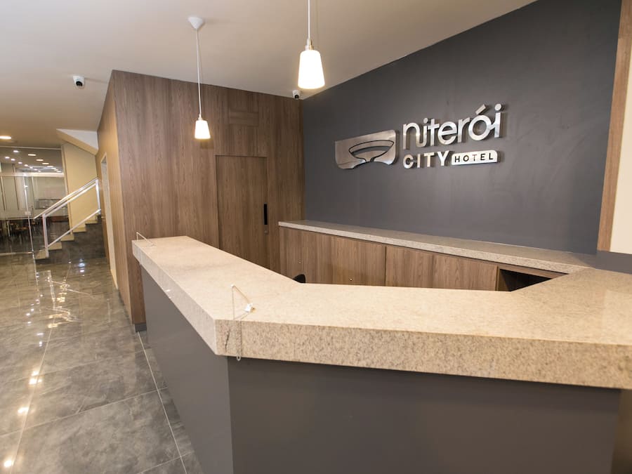 A hotel reception desk with a modern design, a wooden panel wall, and a sign that reads 'Niteroi City Hotel'.