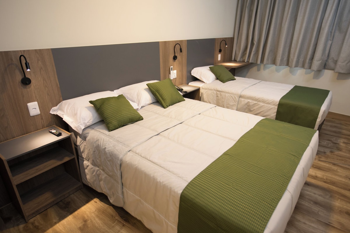 Une chambre d’hôtel avec deux lits, chacun agrémenté d’un oreiller vert, une table de chevet avec un téléphone et une lampe fixée au mur.