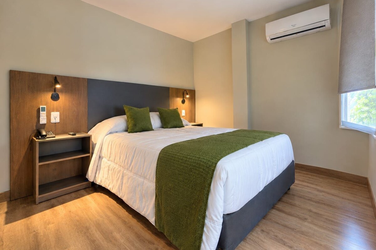 Une chambre d’hôtel avec un lit, des tables de chevet, un climatiseur fixé au mur et une fenêtre.