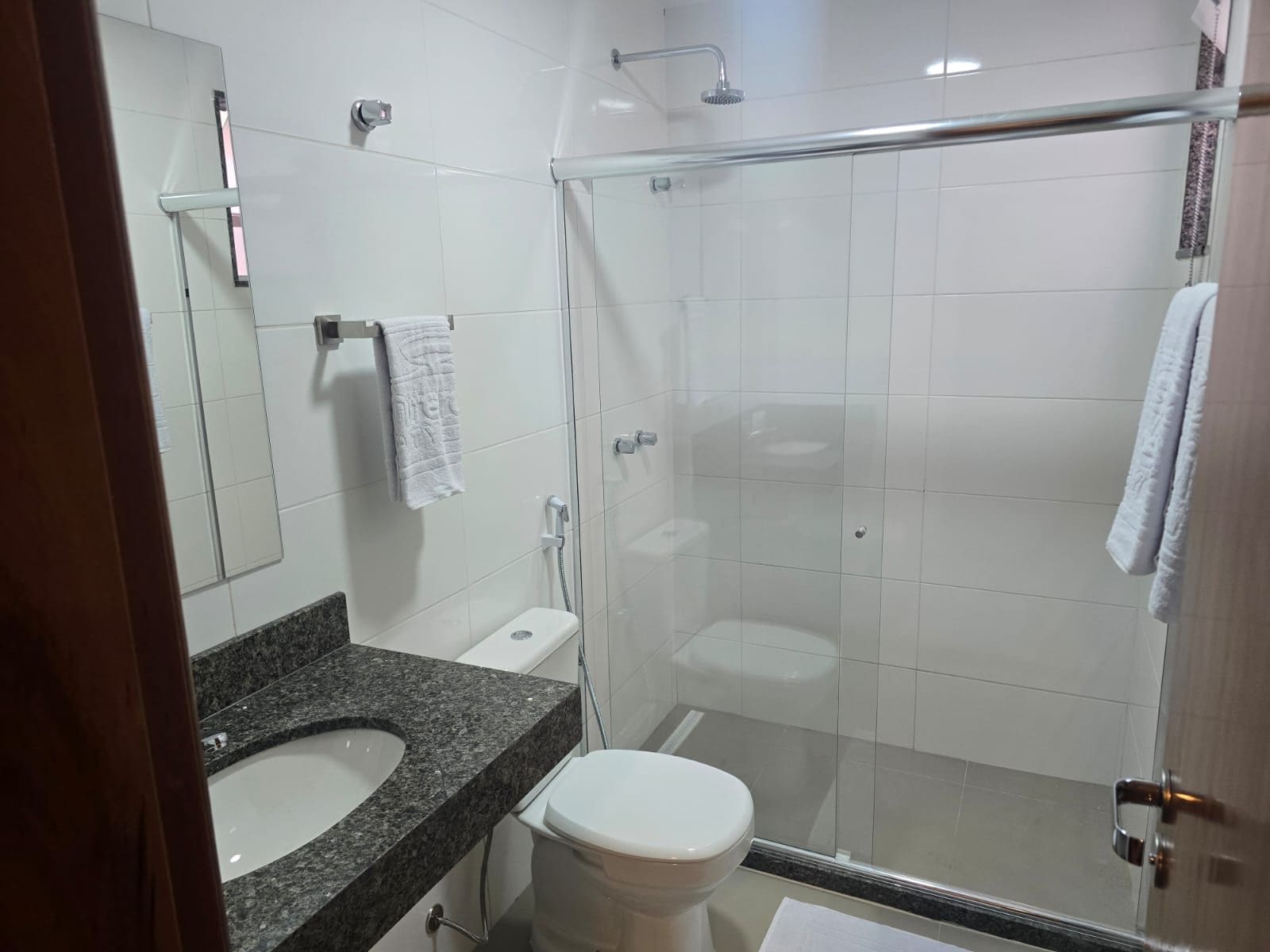 Casa de banho moderna com lavatório de bancada em granito, sanita branca, cabine de duche com vidro e espelho.