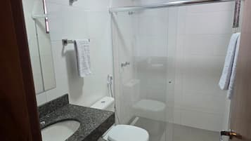 Casa de banho moderna com lavatório de bancada em granito, sanita branca, cabine de duche com vidro e espelho.