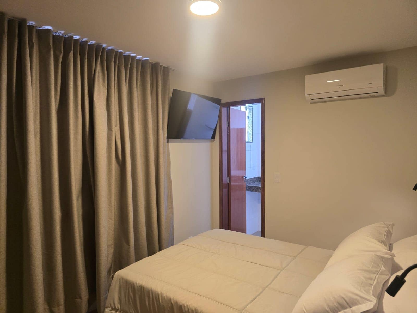 Una habitación de hotel con cama, cortinas, aire acondicionado y televisor.