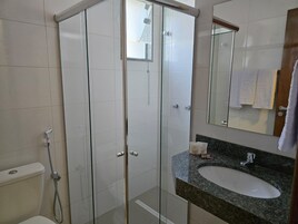 Casa de banho moderna com chuveiro em cabine de vidro, lavatório branco e espelho sobre o lavatório.