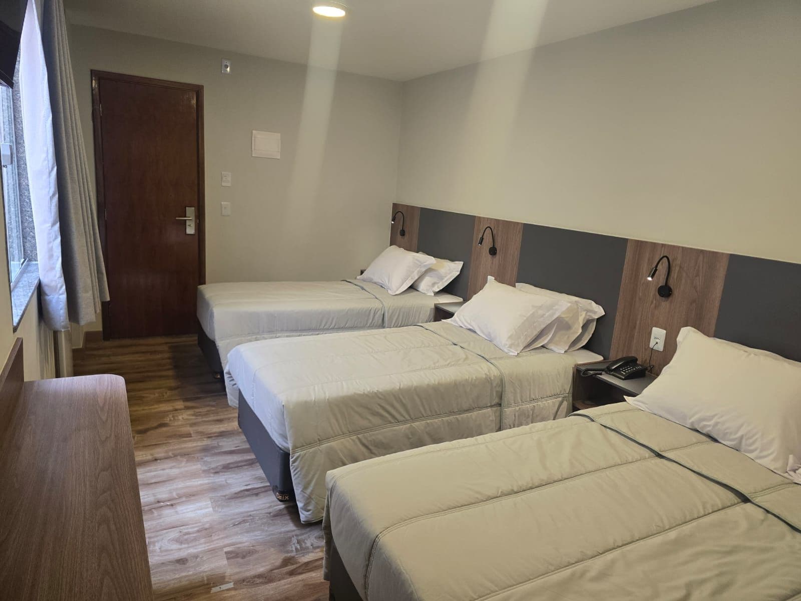 A hotel room with two beds, a desk, and a window with curtains.
