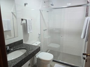 A modern bathroom with a granite countertop sink, a toilet, and a glass-enclosed shower area.