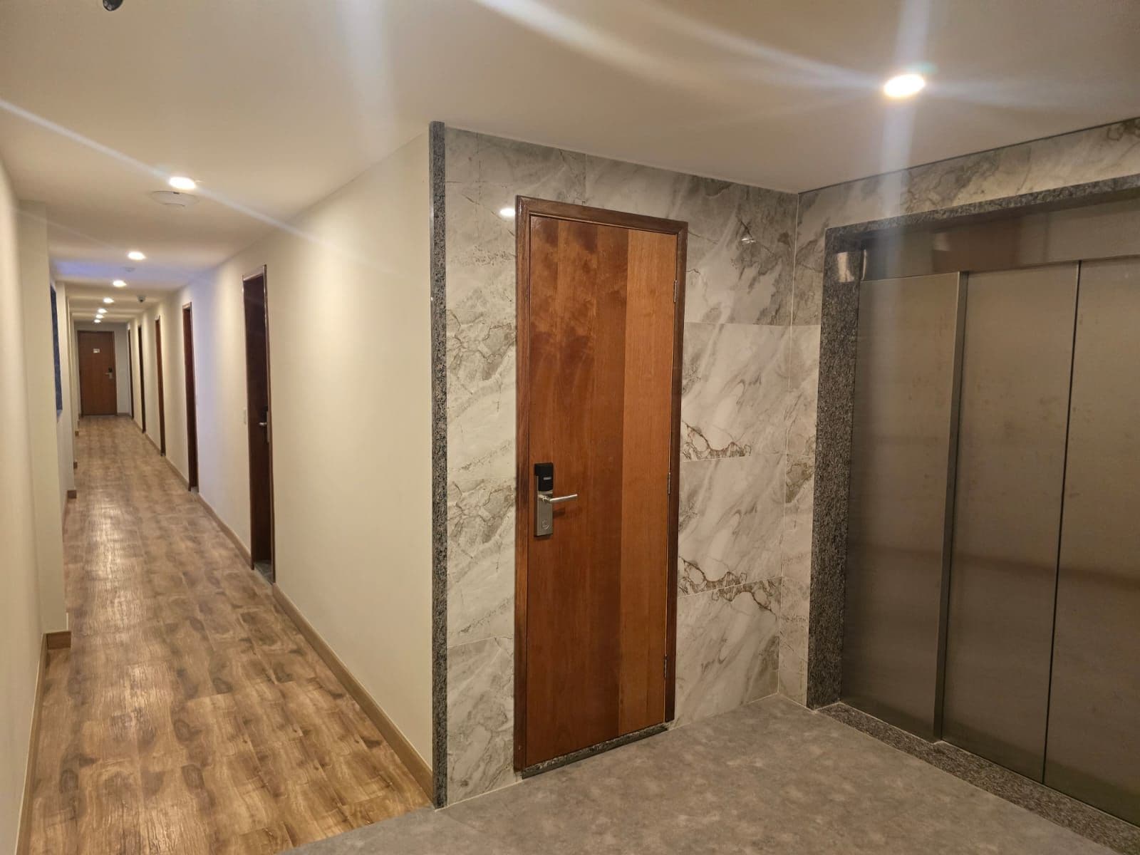 A hotel hallway with a wooden door, marble walls, and a carpeted floor.
