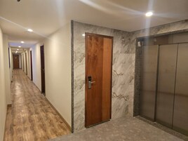 Corredor de hotel com porta de madeira, paredes de mármore e chão coberto de carpete.