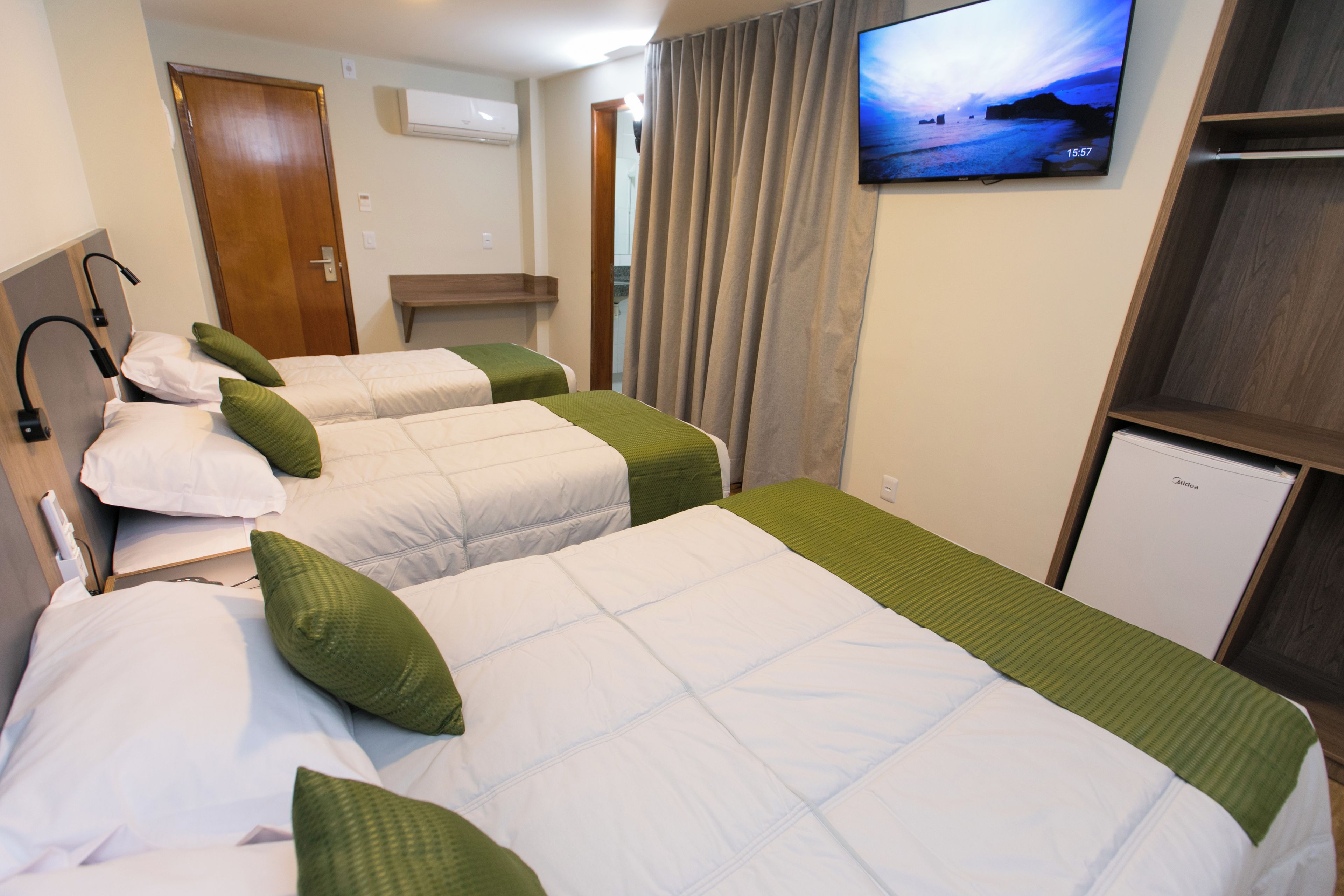 A hotel room with three beds, a television on the wall, and a small refrigerator.