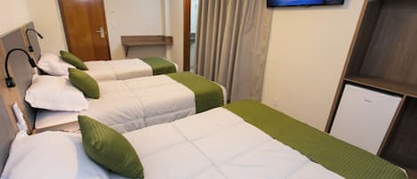 A hotel room with three beds, a television on the wall, and a small refrigerator.