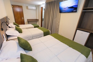 Habitación de hotel con tres camas, un televisor en la pared y un refrigerador pequeño.