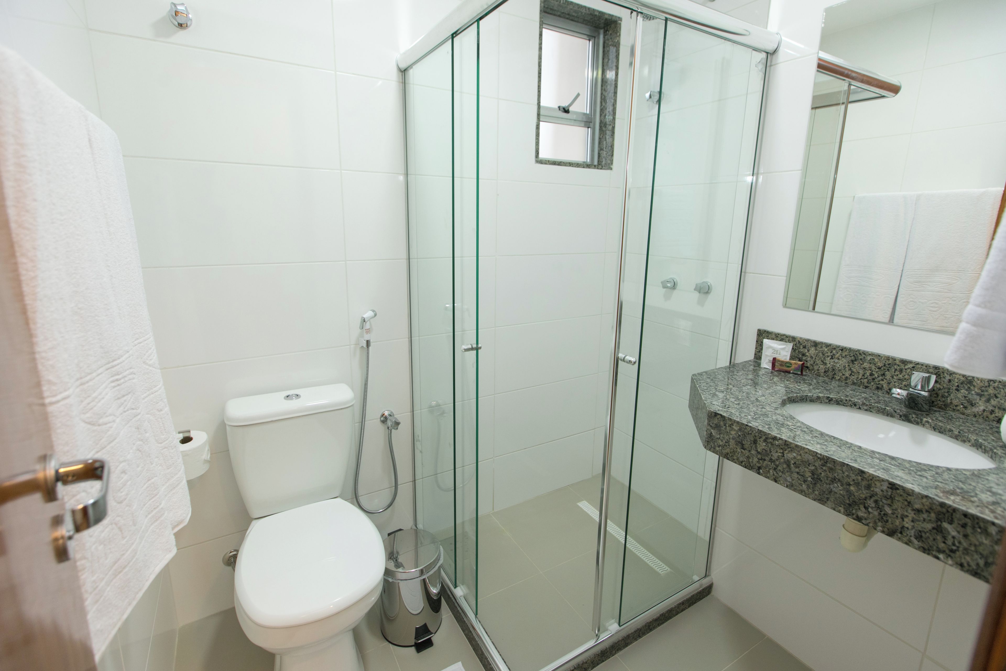 Un baño moderno con ducha envuelta en vidrio, inodoro blanco y lavamanos sobre encimera de granito.
