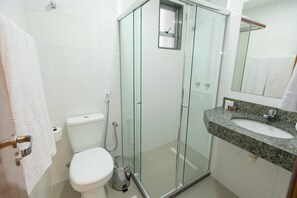 Un baño moderno con ducha envuelta en vidrio, inodoro blanco y lavamanos sobre encimera de granito.