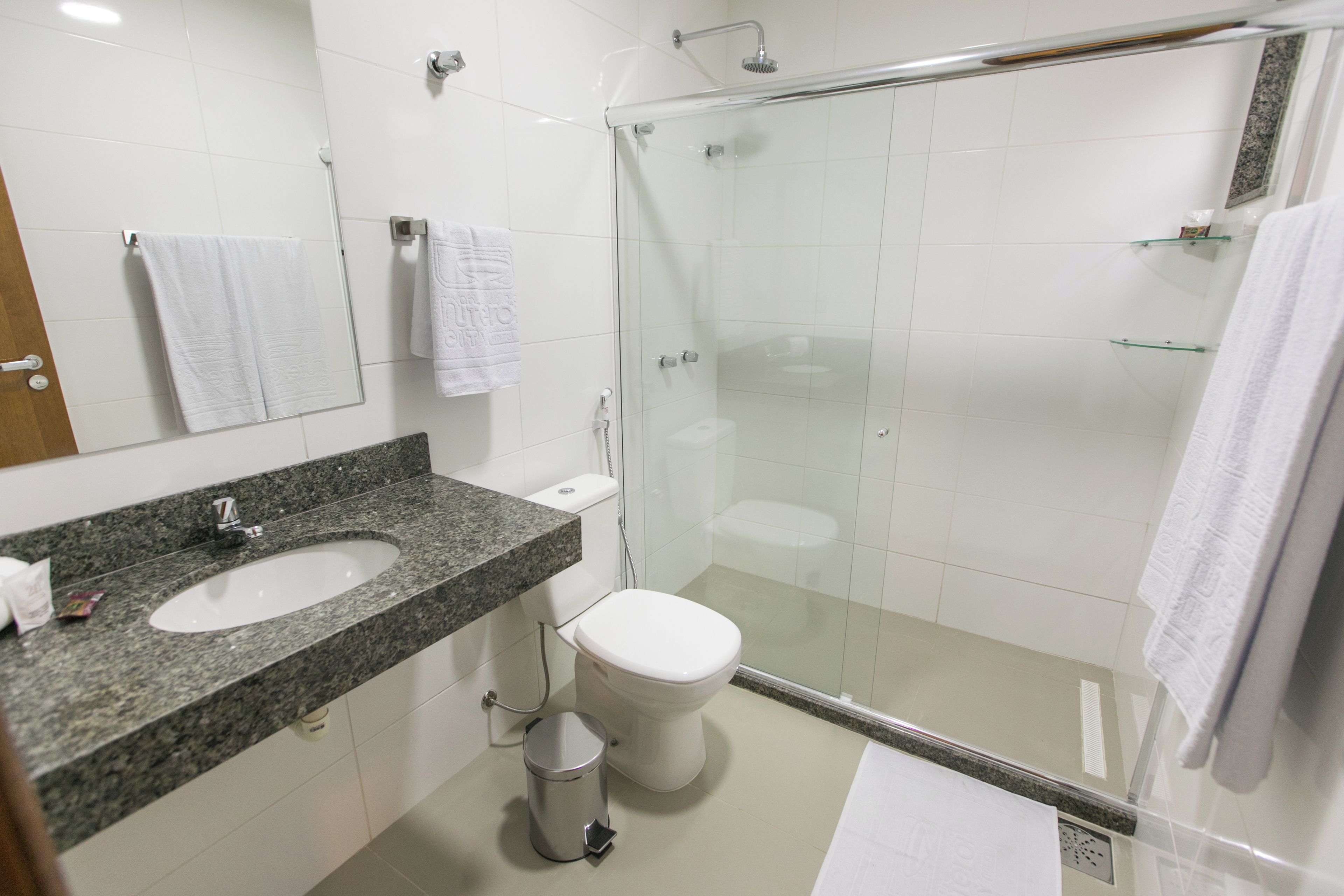 A modern bathroom with a granite countertop sink, a toilet, a glass shower enclosure, and a mirror with a towel hanging on it.