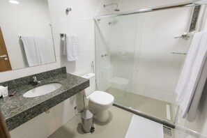 Une salle de bain moderne avec un lavabo surmonté d’un plan de travail en granit, des toilettes, une douche à parois de verre et un miroir sur lequel est accrochée une serviette.