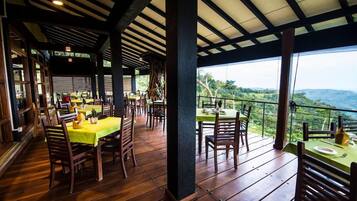 An outdoor dining area with wooden tables and chairs, a covered roof, and a view of the landscape.