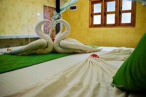 Un lit avec une couvre-lit verte et une couverture blanche. Deux serviettes sont disposées en forme de cœur sur le lit.