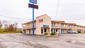 Um motel com um grande letreiro em formato de '6', entrada para a recepção e um estacionamento.