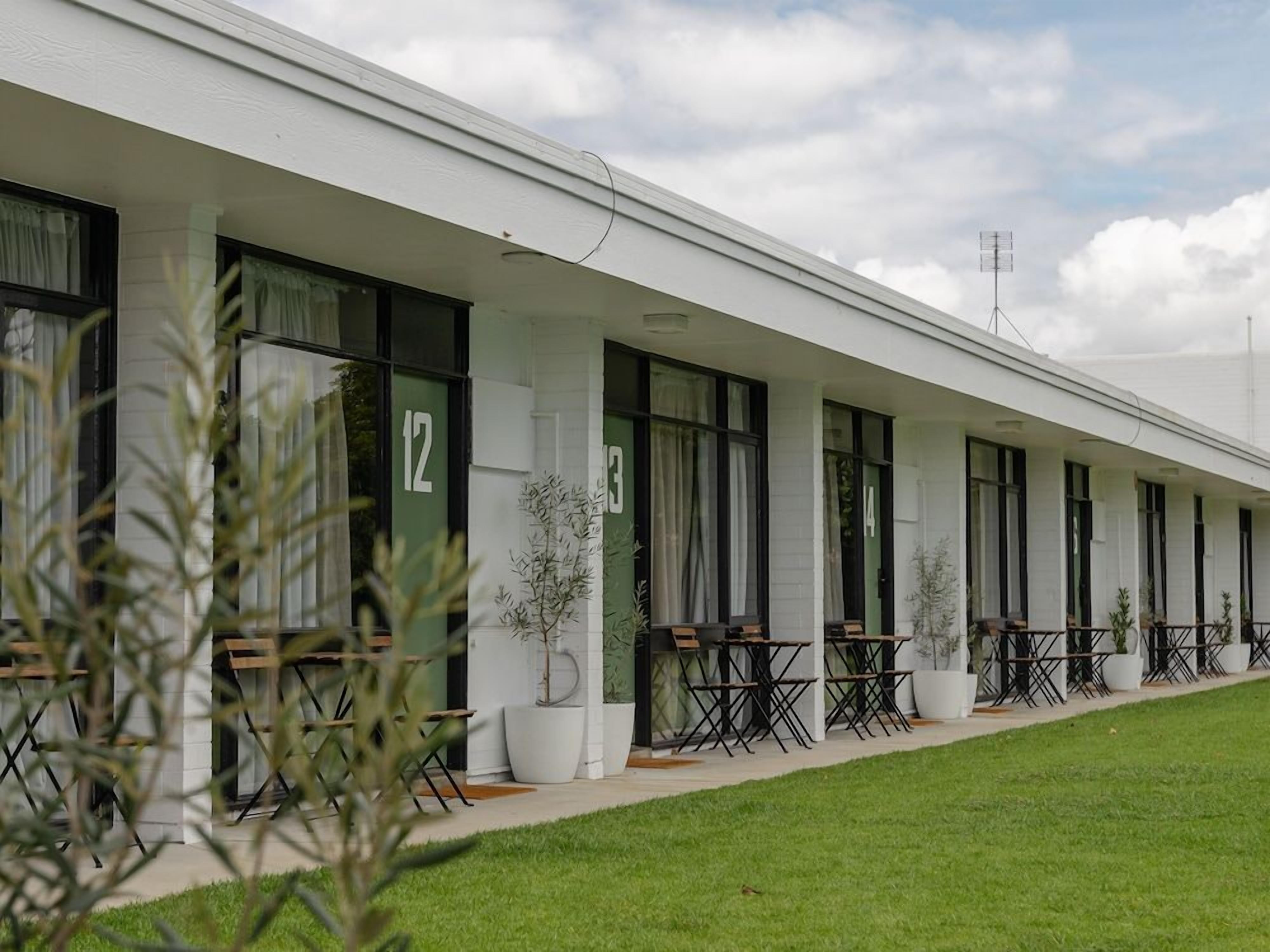 A row of hotel rooms with individual windows, a covered outdoor seating area, and a well-maintained lawn.