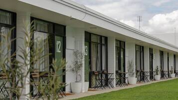A row of hotel rooms with individual windows, a covered outdoor seating area, and a well-maintained lawn.