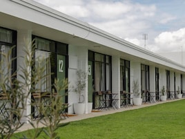 A hotel with a row of rooms, each with a window and a door. There are outdoor seating areas with tables and chairs.