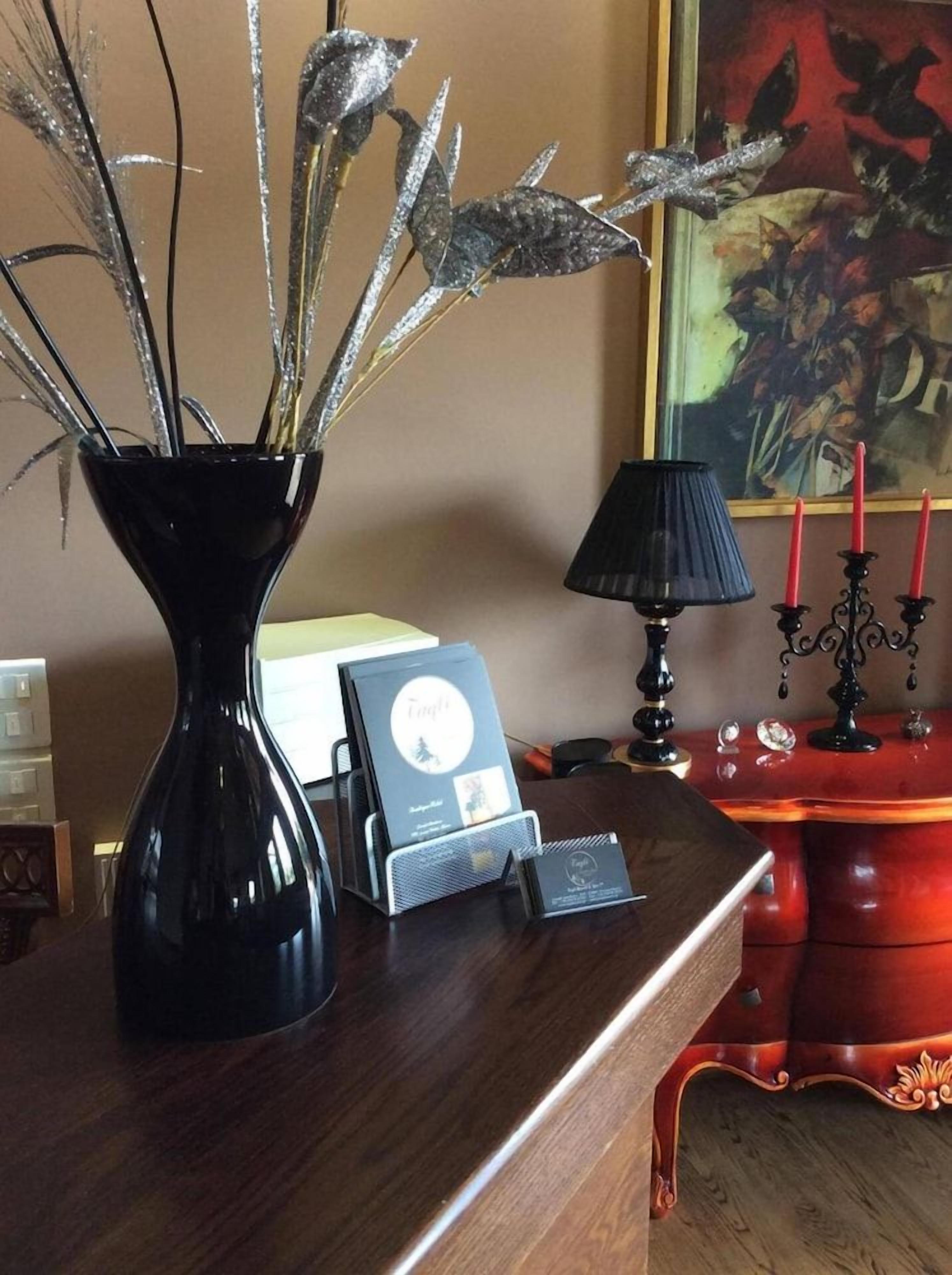 A desk with a black vase containing dried plants, a book, and a small electronic device.