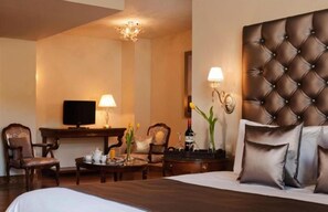 Una habitación de hotel con una cama grande, televisión, escritorio con lámpara y dos sillones.