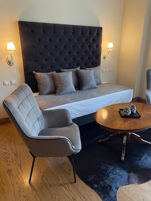 A modern bedroom with a tufted headboard, a grey sofa, a grey armchair, a round coffee table with pinecones, and wall-mounted lamps. - Tagli Resort And Spa (Distomo-Arachova-Antikyra)