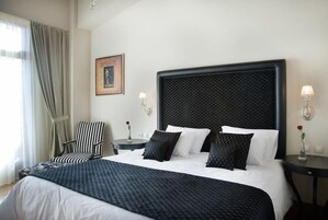 A hotel room with a large bed, a chair, a bedside table, and a wall-mounted picture.