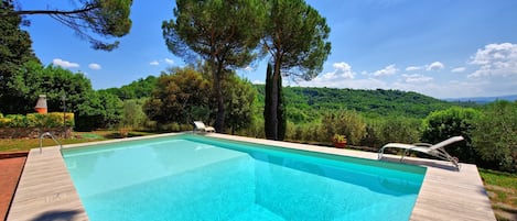 Una piscina rectangular con cubierta de madera, rodeada de árboles y vistas a un paisaje montañoso.