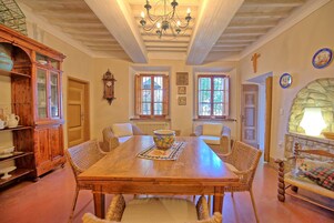 Un comedor con una mesa de madera, sillas de mimbre, una araña y una chimenea de piedra.